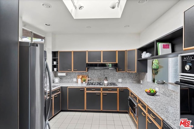 kitchen with light stone countertops, stainless steel fridge, gas cooktop, a skylight, and tasteful backsplash