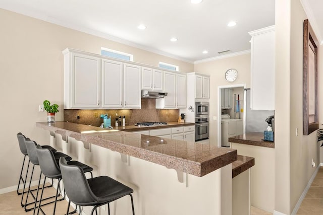 kitchen with white cabinetry, stainless steel appliances, a kitchen breakfast bar, kitchen peninsula, and washer and dryer