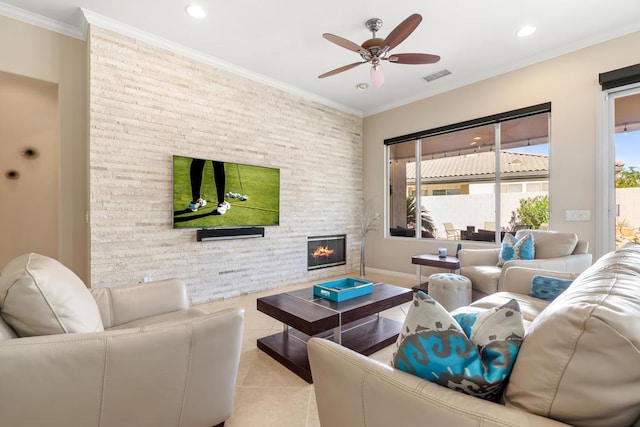 living room with a stone fireplace, ceiling fan, crown molding, and light tile patterned flooring