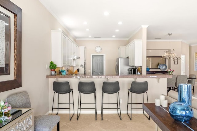 kitchen featuring a kitchen breakfast bar, crown molding, a notable chandelier, white cabinetry, and hanging light fixtures