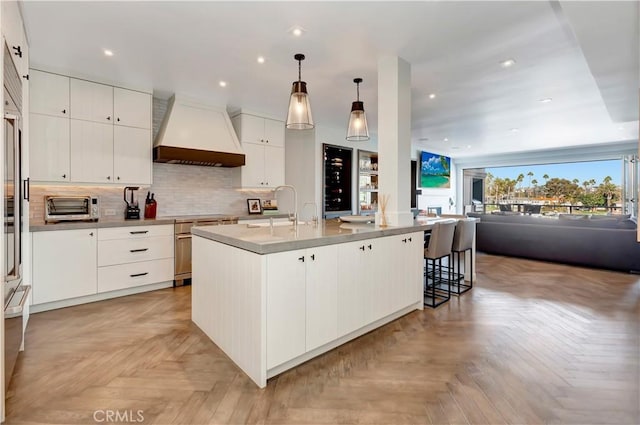 kitchen featuring open floor plan, a toaster, custom range hood, decorative backsplash, and a sink