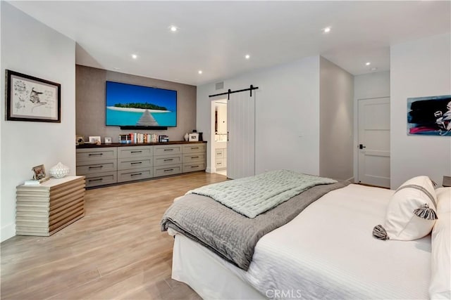 bedroom with ensuite bath, a barn door, and light hardwood / wood-style flooring