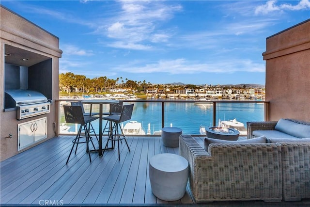 wooden terrace with area for grilling, an outdoor fire pit, and a water view