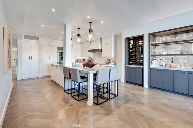 kitchen featuring light parquet flooring, a large island with sink, pendant lighting, a kitchen bar, and white cabinets