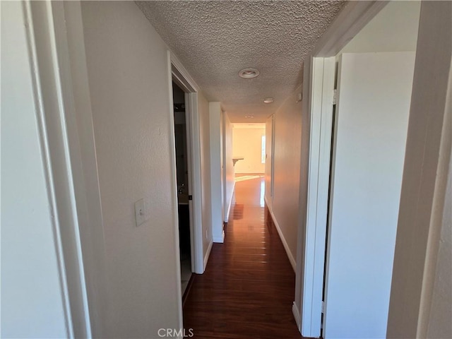 hallway with a textured ceiling and dark hardwood / wood-style floors