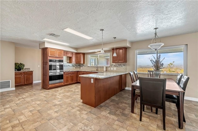 kitchen featuring kitchen peninsula, decorative backsplash, stainless steel double oven, and hanging light fixtures