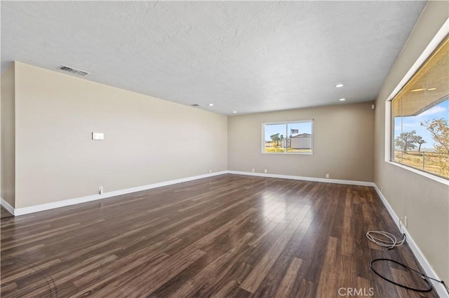 spare room featuring a textured ceiling, a wealth of natural light, and dark wood-type flooring