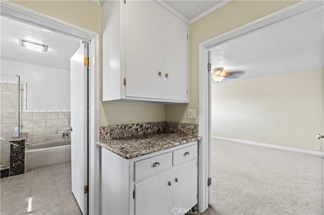 kitchen with light carpet, dark stone counters, crown molding, a textured ceiling, and white cabinetry