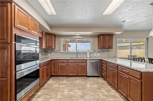 kitchen featuring kitchen peninsula, tasteful backsplash, stainless steel appliances, sink, and pendant lighting