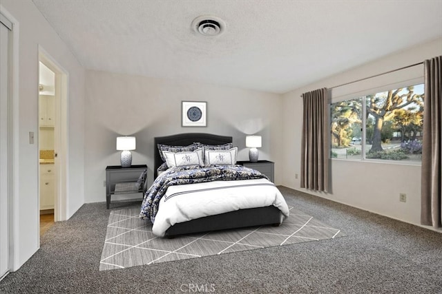 carpeted bedroom with ensuite bathroom and a textured ceiling