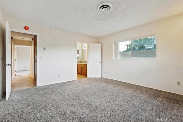 unfurnished bedroom featuring light carpet, a textured ceiling, and ensuite bath