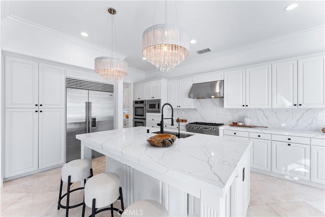 kitchen with built in appliances, a notable chandelier, ventilation hood, and an island with sink