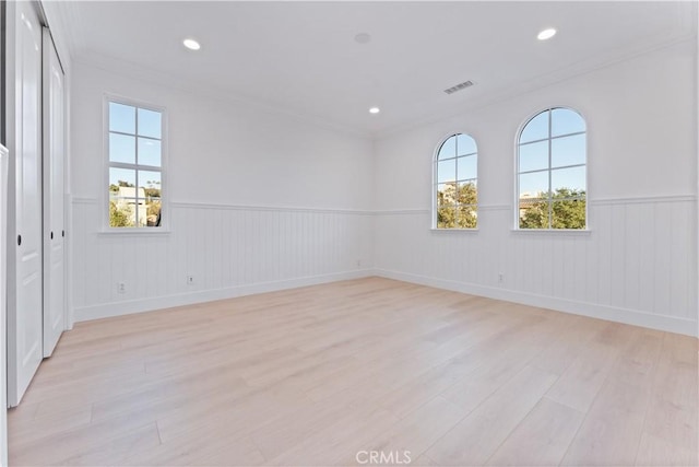 empty room with plenty of natural light, ornamental molding, and light hardwood / wood-style flooring