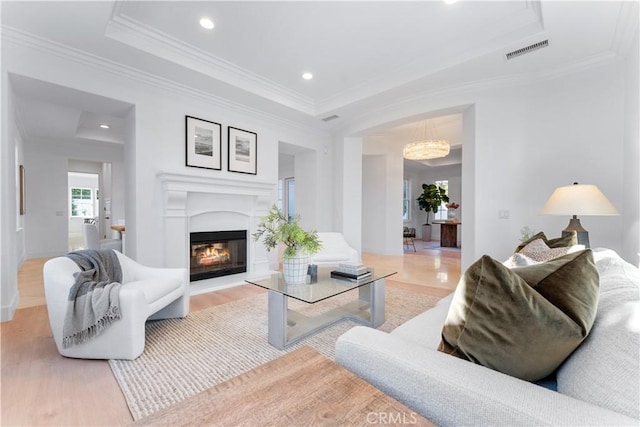 living room featuring a raised ceiling, ornamental molding, a notable chandelier, and light wood-type flooring