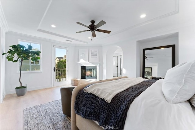 bedroom featuring access to outside, a raised ceiling, light hardwood / wood-style flooring, ceiling fan, and ornamental molding