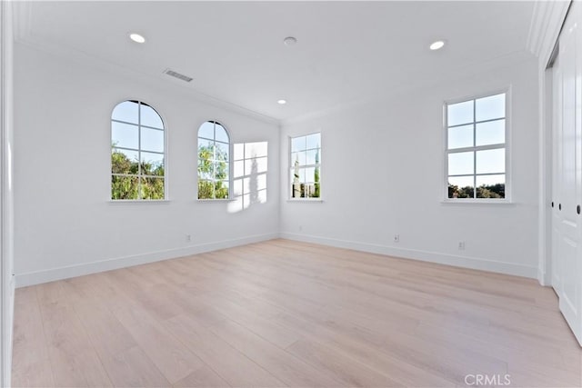 empty room with a wealth of natural light, light hardwood / wood-style floors, and ornamental molding