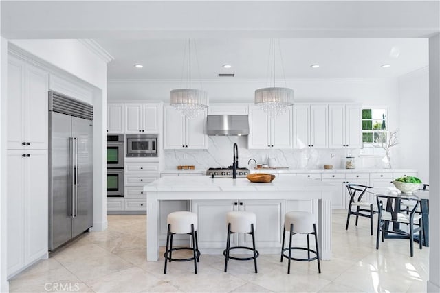 kitchen featuring pendant lighting, a kitchen island with sink, an inviting chandelier, ventilation hood, and built in appliances