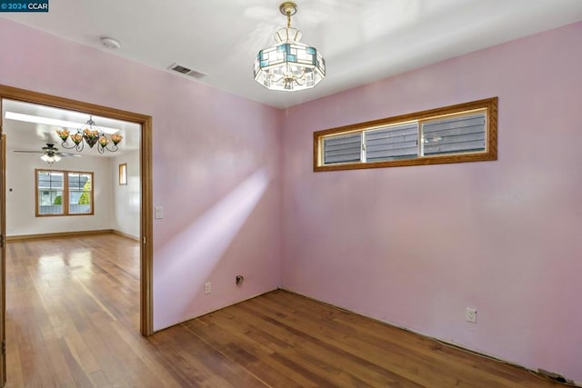 empty room with hardwood / wood-style flooring and ceiling fan with notable chandelier