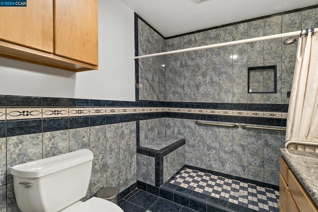 bathroom with a tile shower, vanity, tile walls, tile patterned flooring, and toilet