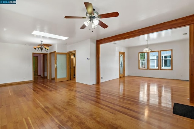 unfurnished living room featuring a skylight, ceiling fan with notable chandelier, and light wood-type flooring