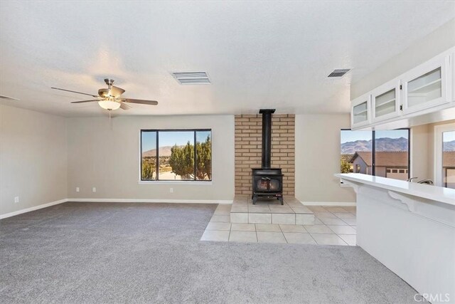 unfurnished living room featuring light carpet, a textured ceiling, a wood stove, and ceiling fan