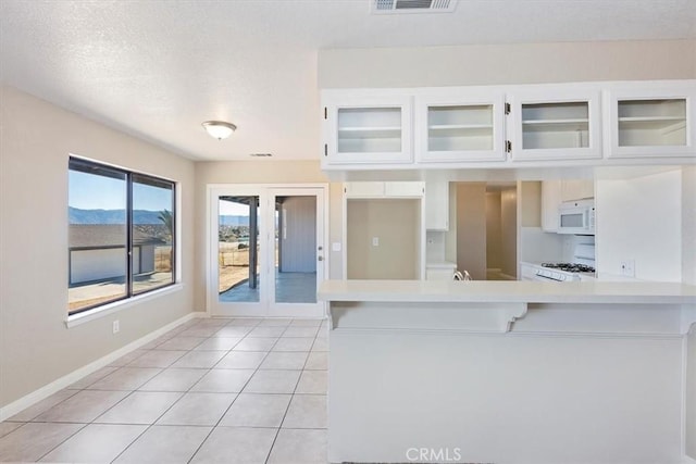 kitchen with kitchen peninsula, white cabinets, light tile patterned flooring, and white appliances