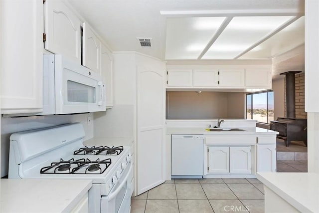 kitchen featuring a wood stove, white cabinetry, sink, white appliances, and light tile patterned floors