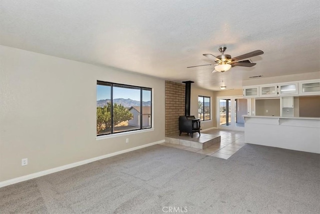 unfurnished living room featuring a wood stove, a wealth of natural light, and light carpet