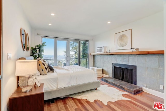 bedroom with a wall mounted air conditioner, wood-type flooring, and a tiled fireplace