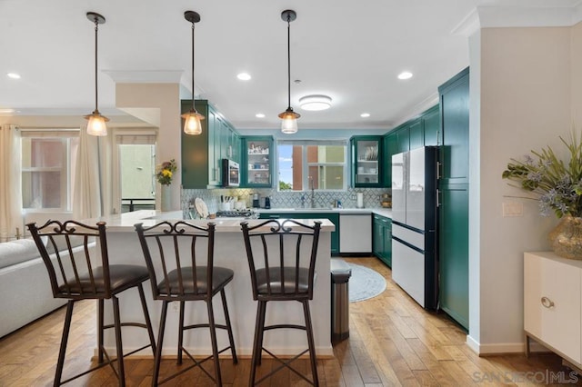 kitchen featuring sink, tasteful backsplash, light wood-type flooring, appliances with stainless steel finishes, and kitchen peninsula