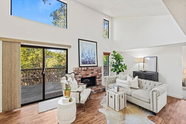 living room with a high ceiling, wood-type flooring, a brick fireplace, and a textured ceiling