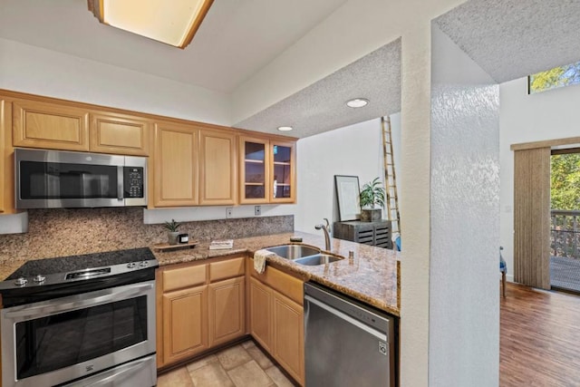 kitchen with tasteful backsplash, sink, kitchen peninsula, stainless steel appliances, and light stone countertops