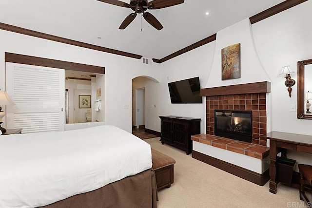 bedroom with a tiled fireplace, ornamental molding, light carpet, and ceiling fan