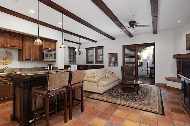 living room featuring a tiled fireplace, sink, ceiling fan with notable chandelier, and beamed ceiling