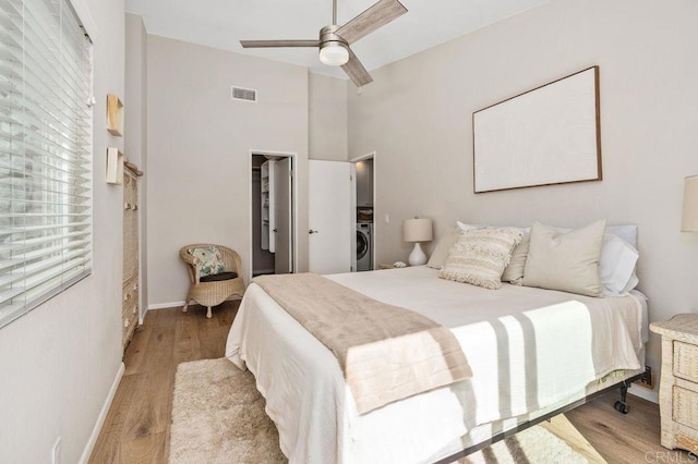 bedroom featuring washer / clothes dryer, a walk in closet, ceiling fan, and light hardwood / wood-style flooring