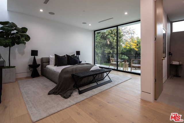 bedroom featuring connected bathroom, a wall of windows, light hardwood / wood-style floors, and access to outside