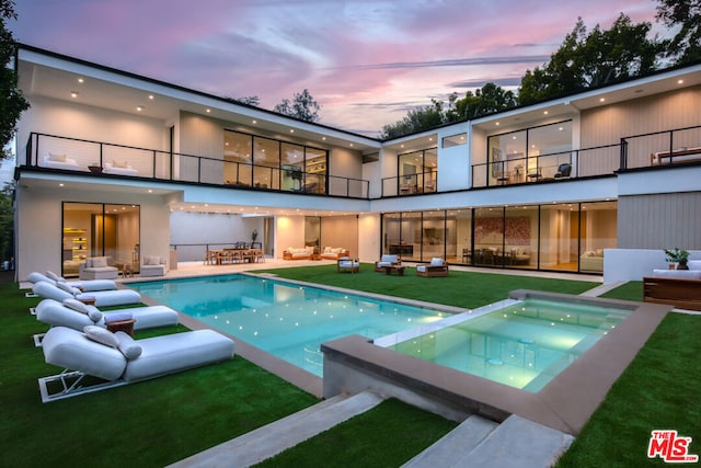 back house at dusk featuring an outdoor hangout area, a swimming pool with hot tub, a balcony, and a patio