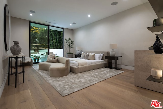 bedroom with access to exterior, a wall of windows, and light hardwood / wood-style flooring