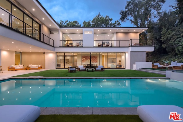 back house at dusk with an outdoor living space, a balcony, and a patio