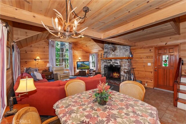 dining space featuring vaulted ceiling with beams, a notable chandelier, wooden walls, a fireplace, and wood ceiling