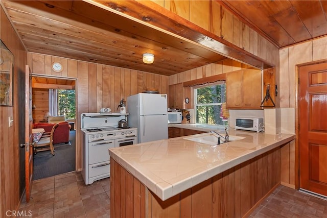 kitchen with sink, white appliances, wooden walls, wooden ceiling, and kitchen peninsula