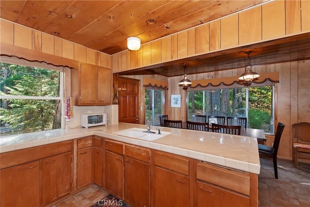 kitchen with kitchen peninsula, wooden walls, tile counters, and plenty of natural light