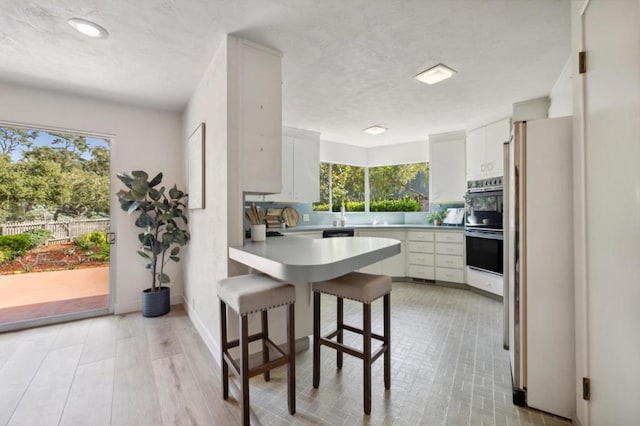 kitchen with multiple ovens, white cabinets, and a kitchen bar