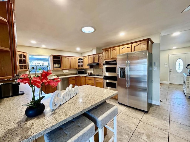 kitchen featuring light stone countertops, kitchen peninsula, a breakfast bar, light tile patterned floors, and appliances with stainless steel finishes