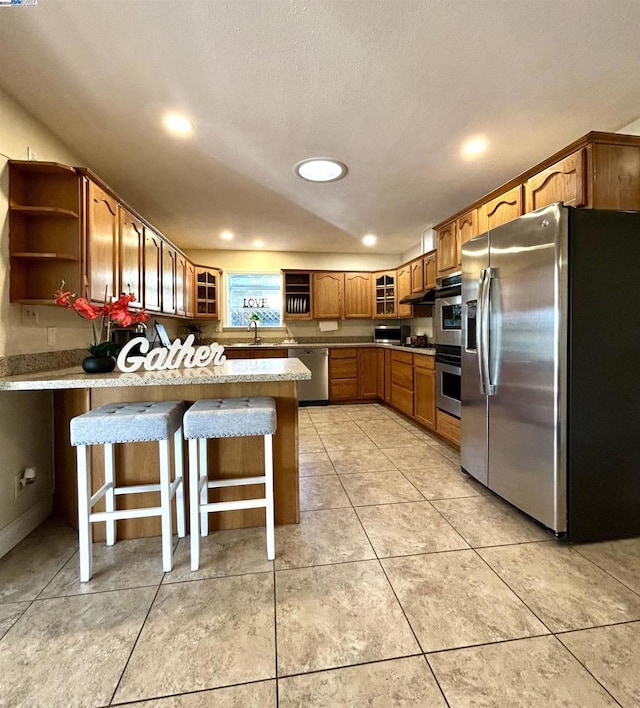 kitchen with sink, a textured ceiling, a breakfast bar, light tile patterned floors, and appliances with stainless steel finishes