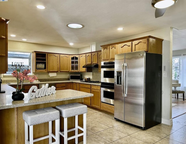 kitchen featuring a breakfast bar, appliances with stainless steel finishes, light tile patterned floors, and a wealth of natural light