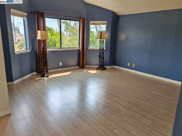 empty room with vaulted ceiling and hardwood / wood-style flooring