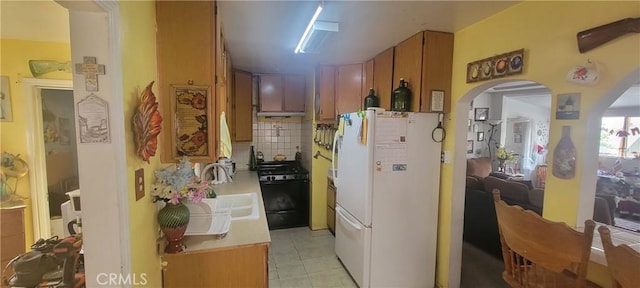 kitchen featuring backsplash, black range, sink, light tile patterned floors, and white fridge