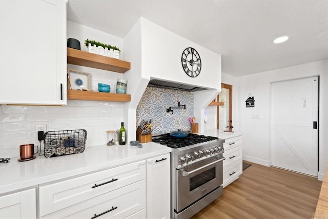 kitchen with white cabinets, backsplash, stainless steel stove, and light hardwood / wood-style flooring