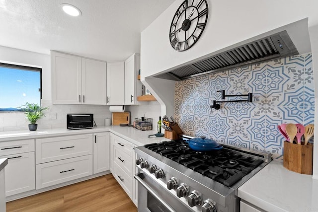 kitchen with decorative backsplash, custom exhaust hood, stainless steel range, light hardwood / wood-style flooring, and white cabinets